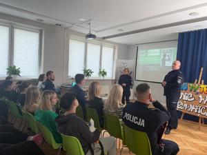 dwoje policjantów na środku sali podczas spotkania z młodzież a w tle ekran