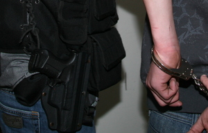 broń w kaburze na pasie policjanta obok dłoń w kajdankach