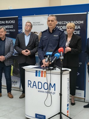 grupa osób podczas konferencji prasowej przy mikrofonie policjant