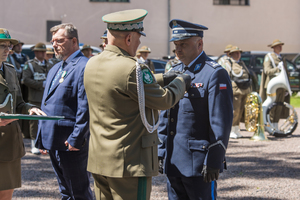 męzczyzna w zielonym mundurze stoi tyłem i wręcza medal policjantowi
