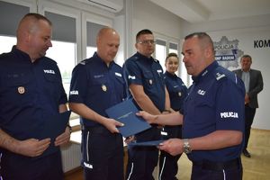 komendant podaje teczkę policjantowi i gratuluje mu obok kolejni mundurowi