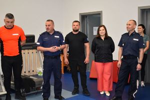 dwaj policjanci w mundurach dwaj w strojach sportowych oraz pracownica komendy