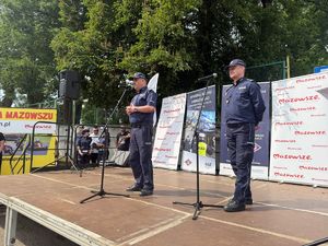 Na scenie stoi dwóch policjantów, jeden mówi do mikrofonu. W tle widać ścianki z logotypami.