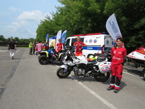Trzech młodych chłopaków ubranych na czerwono, obok nich znajduje się quad, bus, motocykl.
