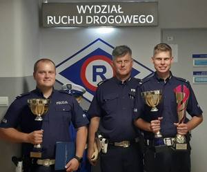trzej policjanci dwóch z nich trzyma w dłoni puchary
