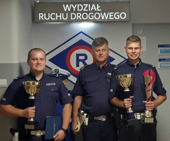 trzej policjanci dwóch z nich trzyma w dłoni puchary