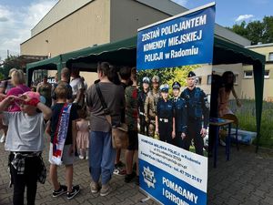 grupa osób stojacych przed namiotem tyłem do aparatu po prawej baner z napisem zostań policjantem