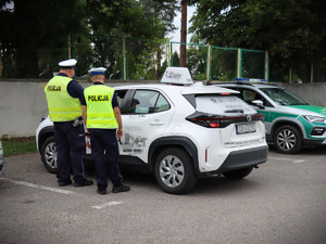 dwaj policjanci przy białym aucie  w tle pojazd strazy granicznej