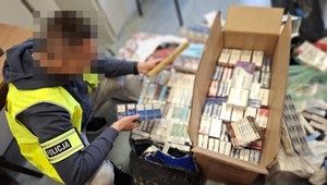 policjant w żółtek kamizelce (zamazana twarz) układa zabezpieczone papierosy