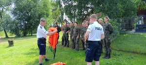 dwaj policjanci trzymaja kamizelki ratunkowe w tle żólnierze podczas szkolenia