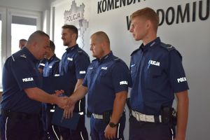 komendant podaje rękę policjantowi gratuluje mu obok 3 policjantów