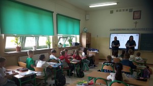 w sali lekcyjnej dzieci siedza w ławkach w tle dwie policjantki na środku sali