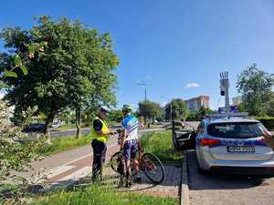 policjant kontrolujący rowerzystę, po prawej stronie radiowóz a na nim system monitoringu mobilnego