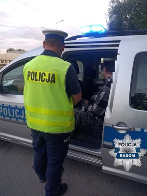 policjant stoi tyłem do aparatu przy radiowozie