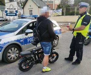 policjant rozmawia  z kierującym rowerem w tle radiowóz