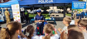 policjantka i grupa dzieci w tle policyjne stoisko profilaktyczne