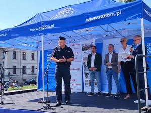 policjant stojacy przy mikrofonie w tle kilka osób