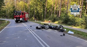 dwa uszkodzone motocykle leżą na jezdni w tle wóz strażacki