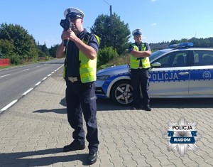 policjanci kontrolujacy prędkośc w tle radiowóz