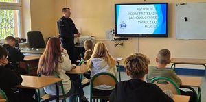 policjant i uczniowie na sali podczas prelekcji