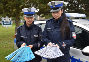 dwie policjantki przy radiowozie trzymaja opaski odblaskowe