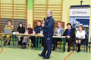 grupa osób w tym mundurowi siedza przy stole w szkole na środku policjant z mikrofonem