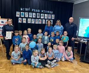 zdjęcie grupowe w sali dzieci ubrane na niebiesko dwoje policjantów i nauczycielki