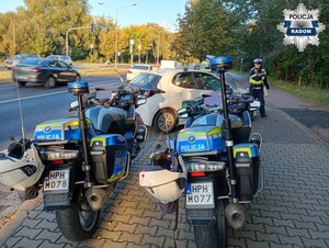 dwa policyjne motocykle w tle policjanci stoją przy białym aucie i kontroluja kierowcę