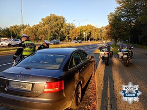 dwaj policjanci przy czarnym aucie, w tle dwa policyjne motocykle