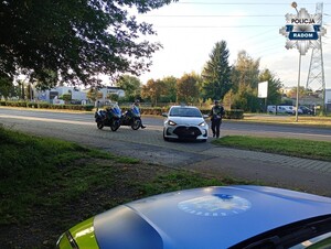 w tle widac dwóch policjantów którzy kontroluja białe auto osobowe