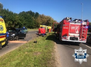 miejsce wypadku, po prawej wóz strażacki na srodku rozbity motocykl, w tle czerwony parawan, widac w tle karetki i rozbite auto osobowe