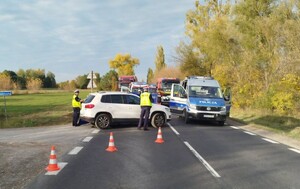 miejsce wypadku, na pierwszym planie białe auto osobowe obok dwóch policjantów w tle radiowóz karetka wóz strażacki