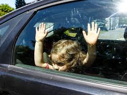 dziecko siedzące wewnątrz pojazdu i opierające się rękami o zamkniętą szybę samochodu