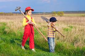 na zdjęciu widoczna jest dziewczynka i młodszy chłopiec, którzy idą przez pole, niosą w rękach narzędzia do prac w polu