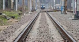 na zdjęciu widoczne są tory kolejowe a w oddali rozmazany przód nadjeżdżającego pociągu