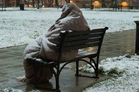 grafika przedstawia osobę siedzącą na ławce przykryta kocem i zasypaną śniegiem