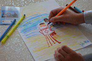 Kartka papieru na której dziecko rysuje czerwoną kredką ratownika nad wodą.