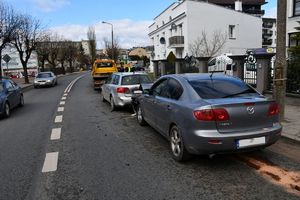 Fotografia kolorowa: na ulicy stoją dwa auta a przed nimi pojazd holujący.