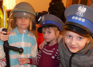 Fotografia kolorowa: trzy dziewczynki w czapkach policyjnych.