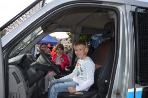 Fotografia kolorowa. Na zdjęciu widać dzieci w samochodzie policyjnym wraz z profilaktykiem z KPP w Mławie.
