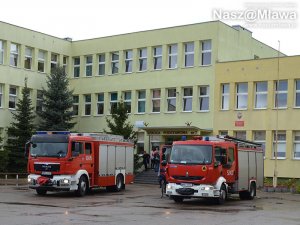Fotografia kolorowa: widzimy SP nr 7 w Mławie, przed którą stoją dwa pojazdy straży pożarnej - ewakuacja uczniów po rozpyleniu substancji drażniącej - gaz.