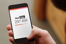 Fotografia kolorowa: widzimy dłoń trzymającą telefon komórkowy - na ekaranie napis KOD BLIK oraz numer sześcio cyfrowy .