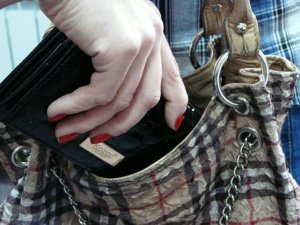 Fotografia kolorowa. Na zdjęciu widoczna damska dłoń trzymająca czarny portfel, który umieszcza w torebce.