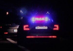 noc, droga, oznakowany samochód policyjny z włączonymi sygnałami świetlnymi.