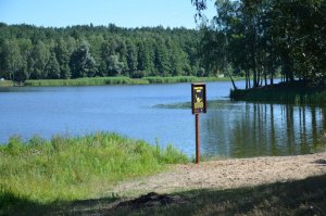 Fotografia kolorowa: na tle zbiornika wodnego Zalew Ruda pow. mławski, widzimy ustawioną tablicę &quot;Czarny punkt wodny&quot;.