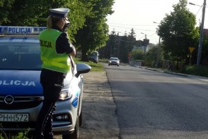 policjantka trzyma urządzenie do pomiaru prędkości na drodze, stoi przy radiowozie