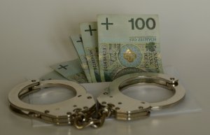 kajdanki policyjne w tle kilka banknotów o nominale 100 zł