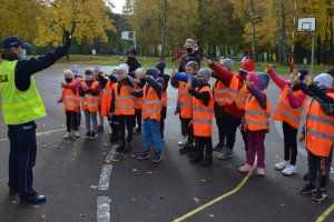 policjantka stoi na boisku przed grupą dzieci, dzieci mają w ręku odblaskowe zawieszki