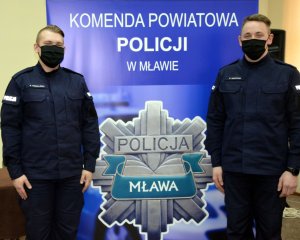 dwóch policjantów stoi na tle baneru mławskiej policji