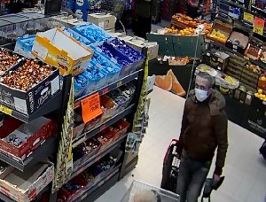Fotografia: kradzież sklepowa, pomiędzy półkami sklepowymi widzimy szczupłego mężczyznę, w kurtce koloru szarego i maseczce na twarzy.